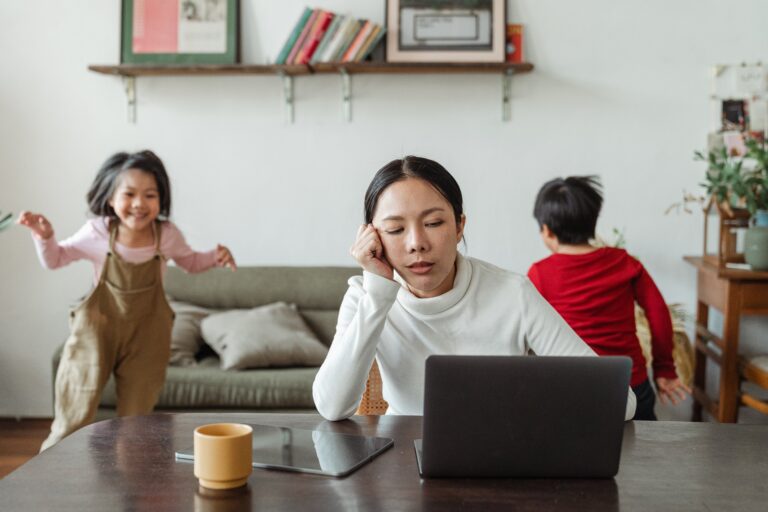 stressd-out-female-mom-working-from-home-with-her-laptop-on-the-table-while-her-childrens-messing-around