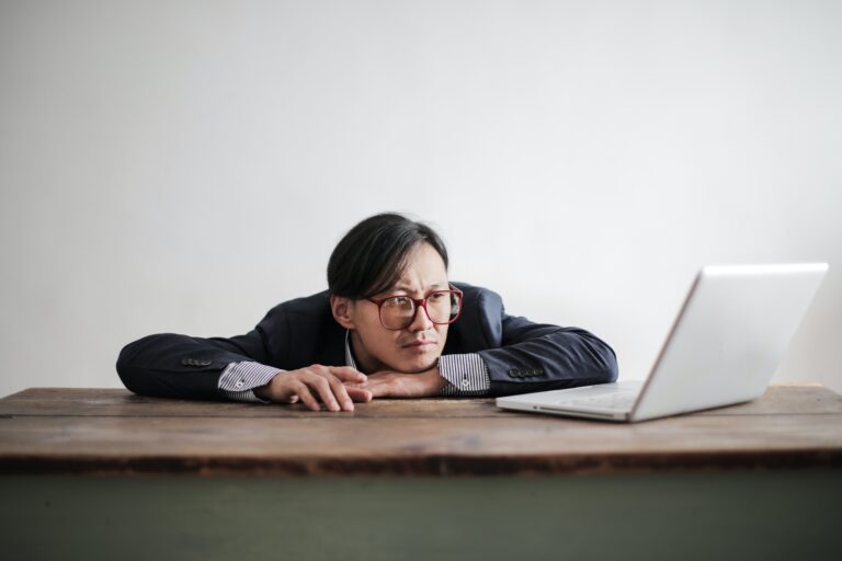 a office man in eustress state with big red round glasses is working on his grey laptop