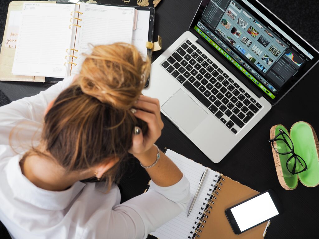 woman has information overload and holds her head as an expression of stress among her work setup