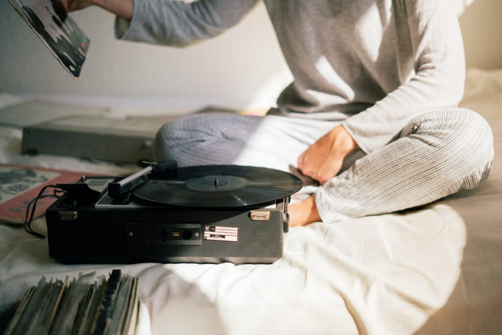 a person is sitting on the bed while picking the record up with the record player playing on the bed