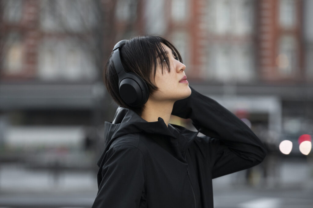 short haired woman is listening to music though her black headphone while looking up to the sky